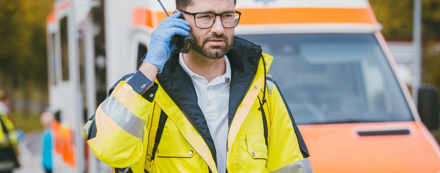 Medic man talking to headquarter via radio in front of ambulance