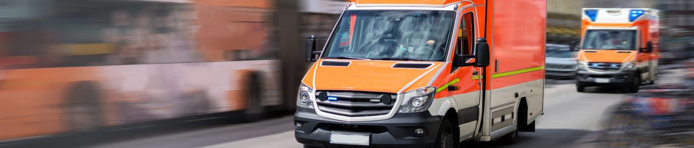two emergency ambulances are driving fast with blue flashing light through the city, panned shot with motion blur